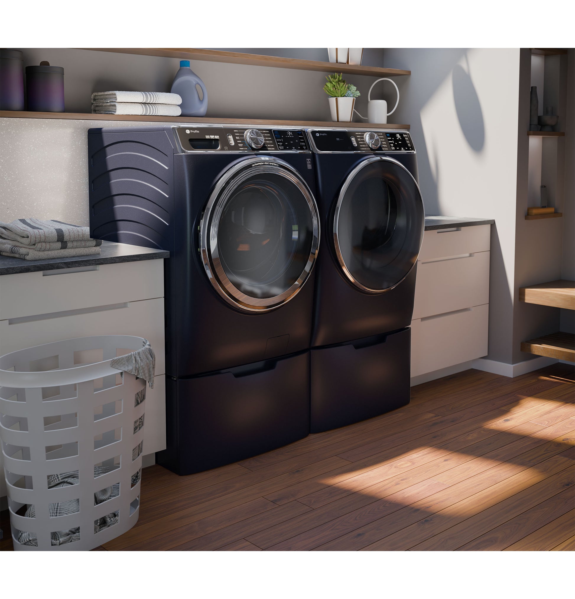 Dark blue smart front load washer and gas dryer set in modern laundry room with wood flooring and white cabinetry
