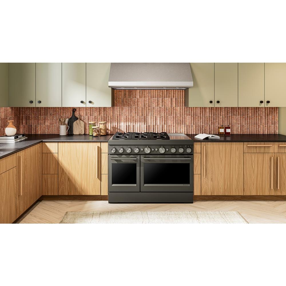 Matte black dual fuel range with six burners and double electric ovens set within modern wood cabinetry and black countertops
