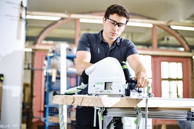 Man wearing safety glasses operating a Festool plungecut saw on wood in a power tools workshop