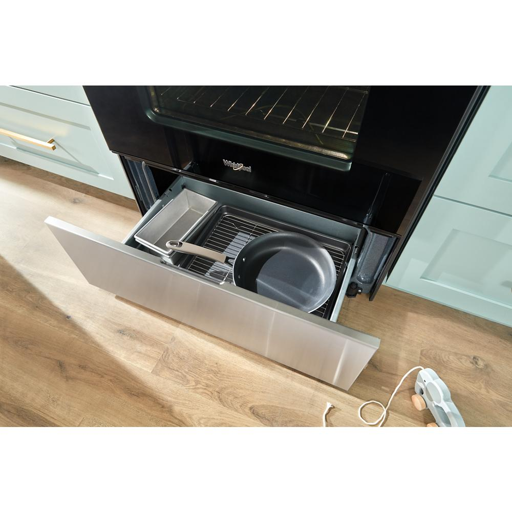 Open warming drawer of stainless steel electric range with skillet and broiler pan inside in kitchen setting