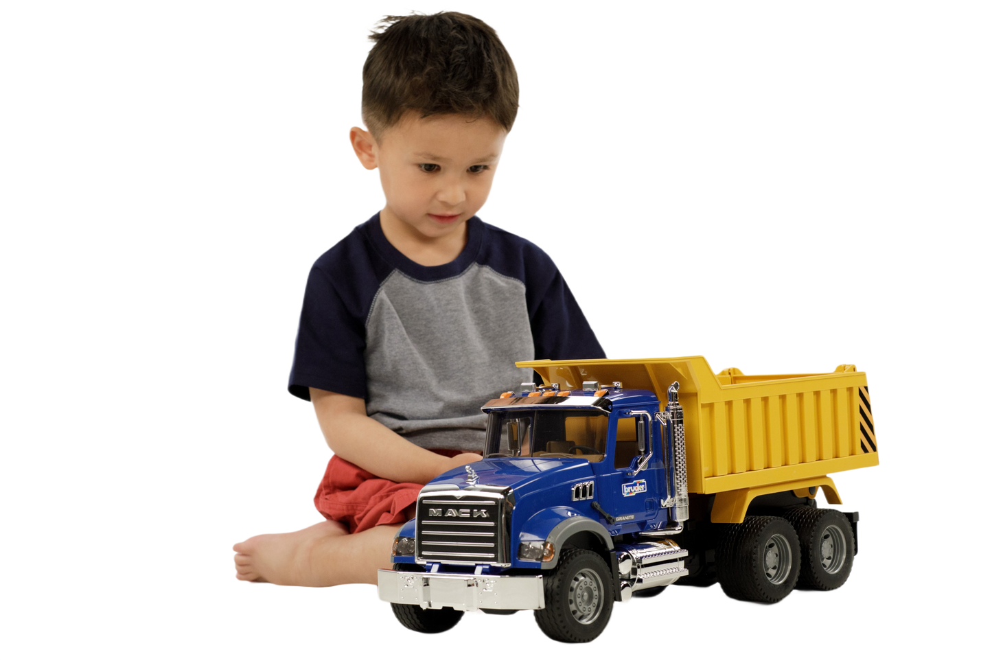 Child playing with a blue and yellow Bruder MACK Granite dump truck toy featuring detailed cab and tilting bed