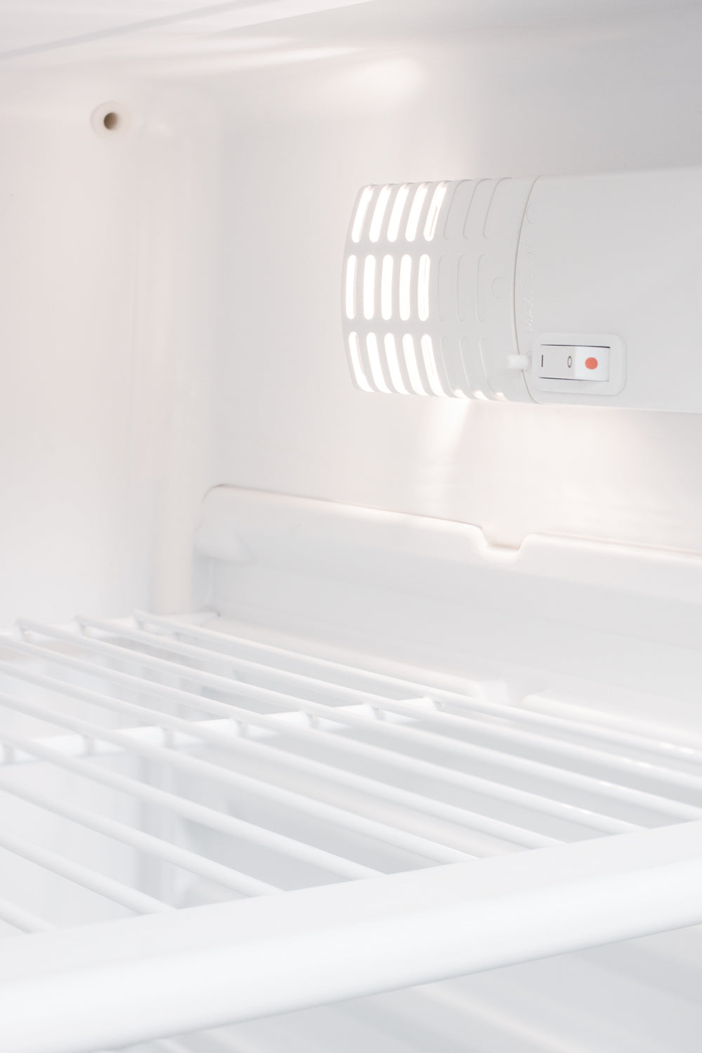 Interior view of white refrigerator shelf with ventilation grills and illuminated control switch in kitchen appliance collection