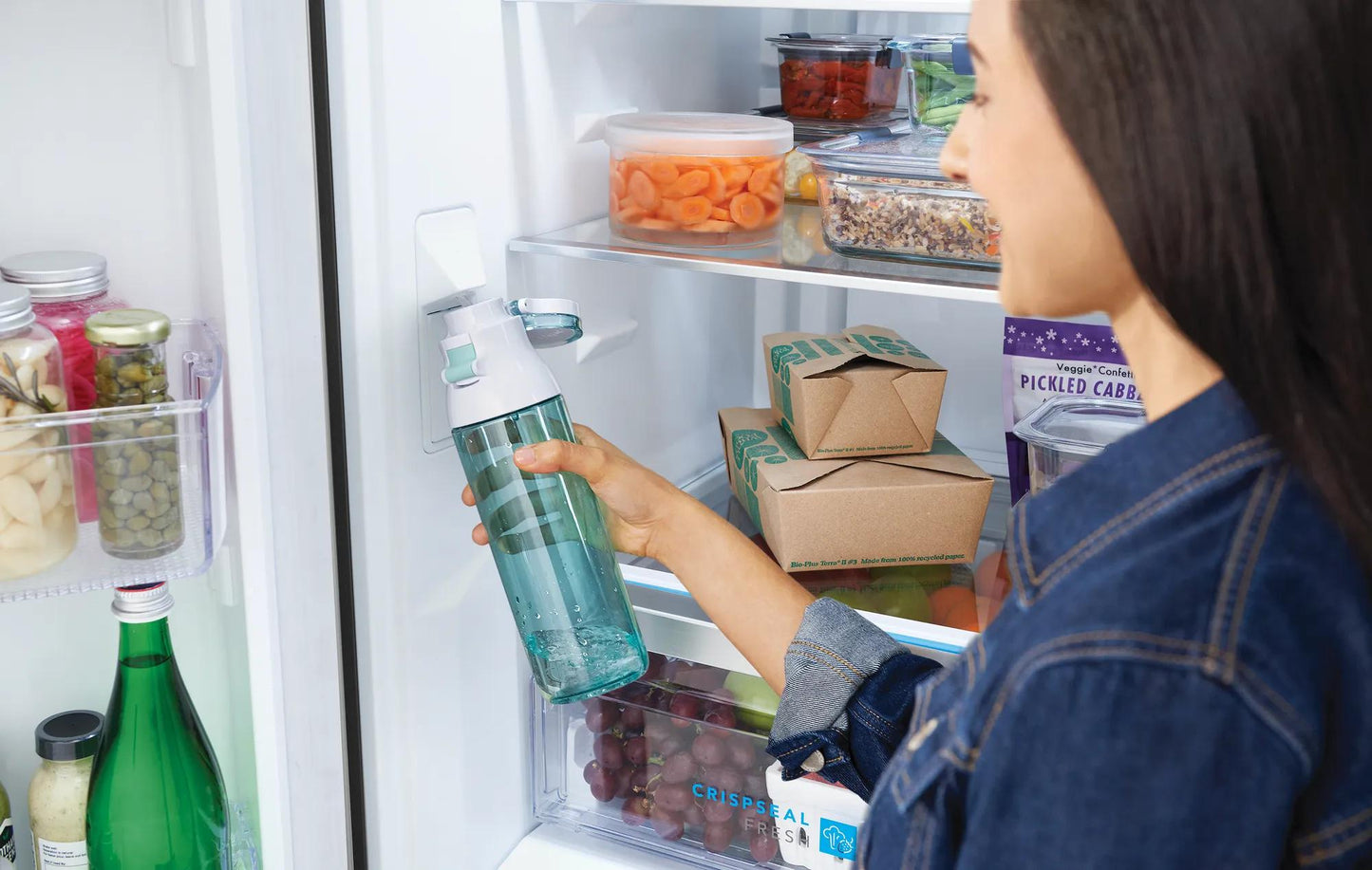 Person placing a clear glass bottle inside a 20 Cu. Ft. French door refrigerator with organized food storage in kitchen setting