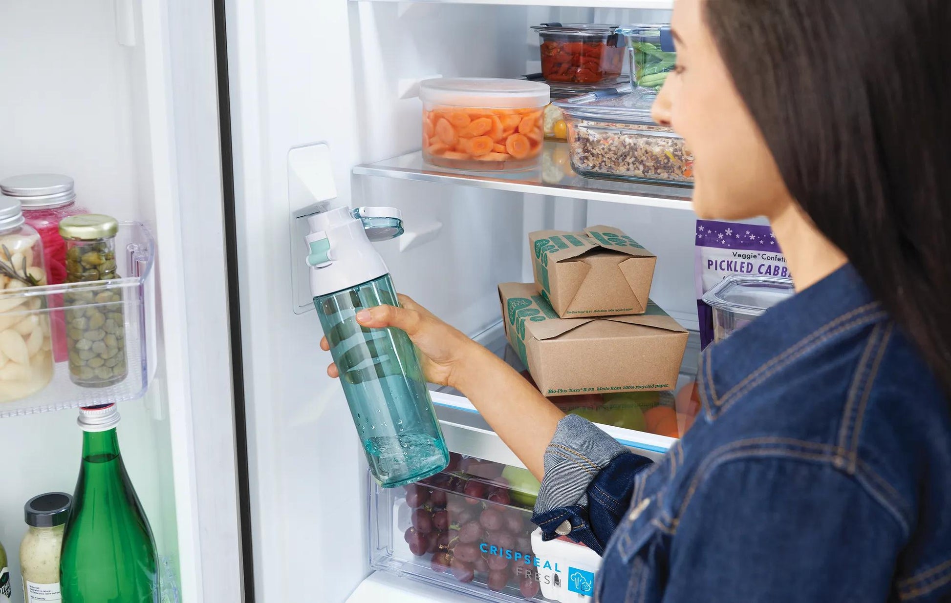 Person placing a clear glass bottle inside a 20 Cu. Ft. French door refrigerator with organized food storage in kitchen setting