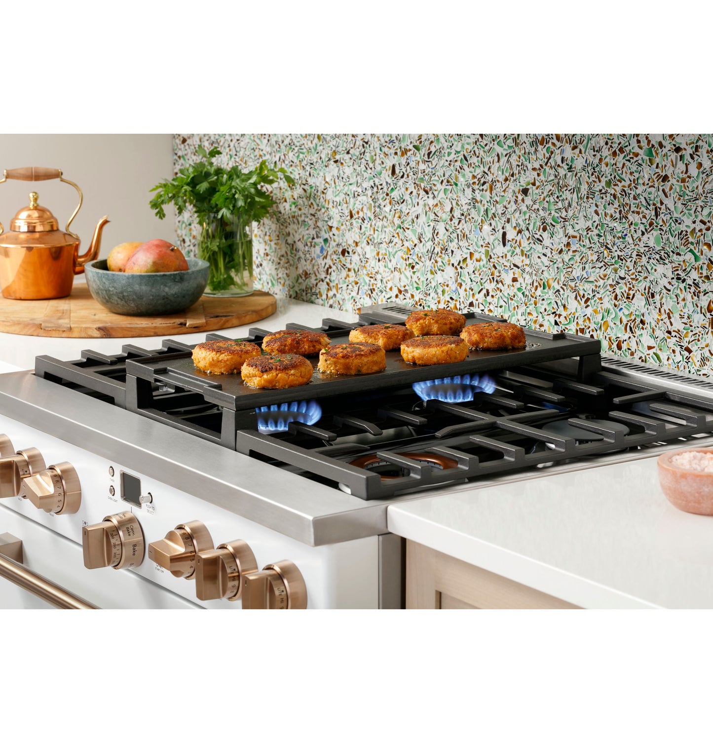 Commercial-style stainless steel gas range with six burners cooking patties on cast iron grates in modern kitchen setting