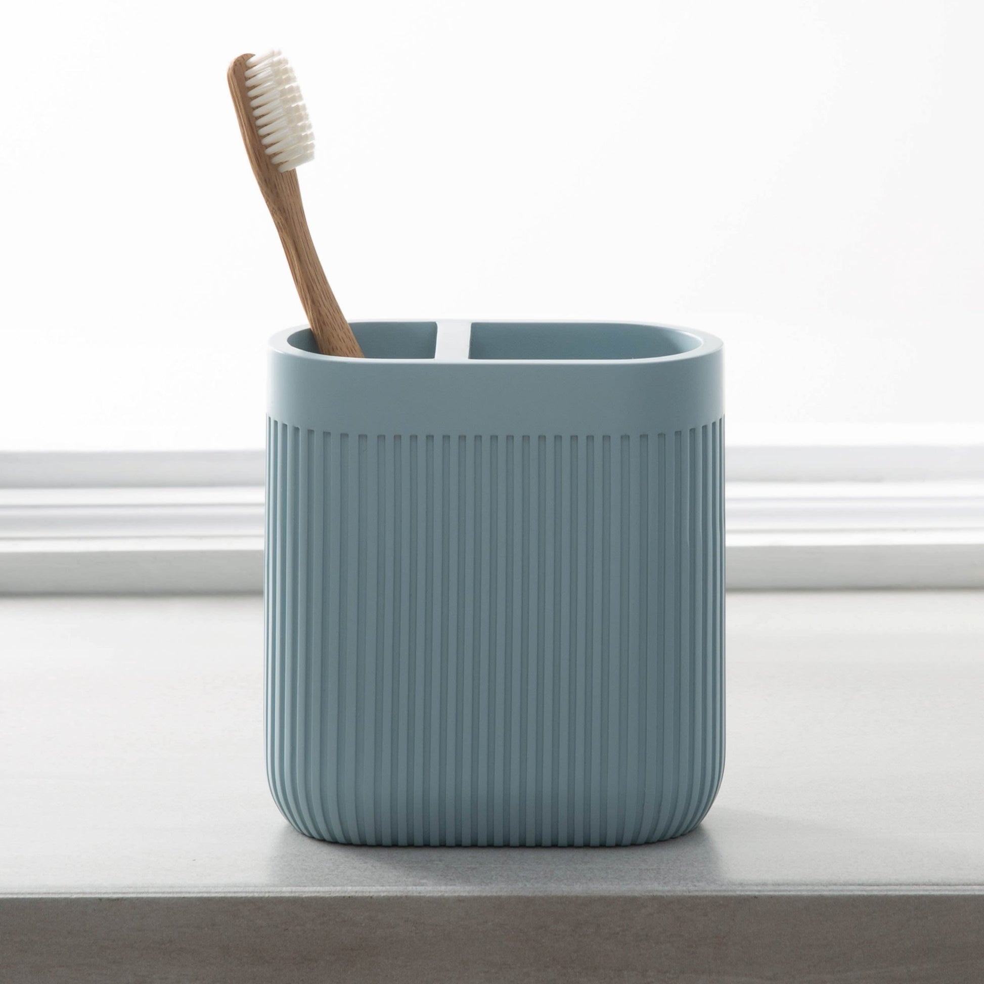 Blue resin toothbrush holder with vertical ridges and divided compartments, placed on bathroom countertop with wooden toothbrush