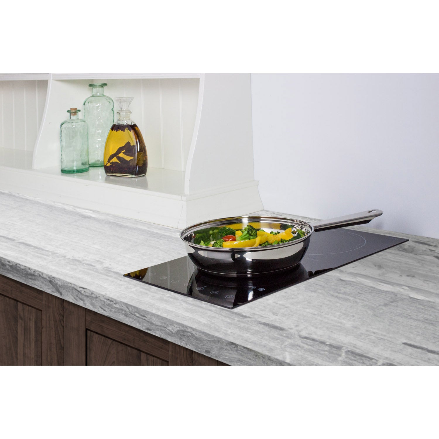12" wide black radiant cooktop with two burners installed in gray stone countertop with stainless steel skillet cooking vegetables