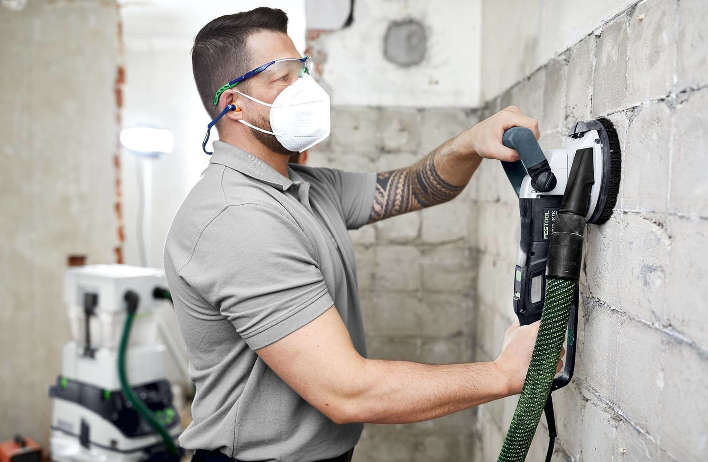 Man wearing safety gear using a power grinder to smooth a concrete wall in a construction setting