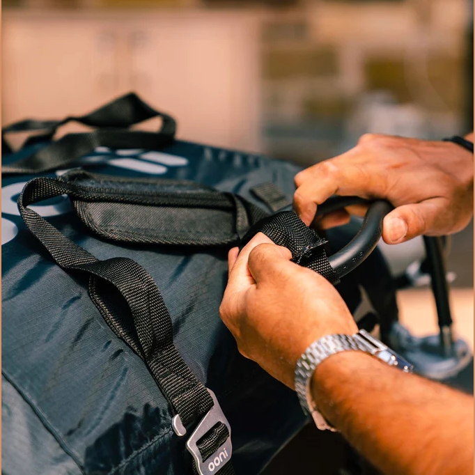 Hands securing adjustable black straps on a polyester carry cover for outdoor pizza ovens in grilling accessories collections