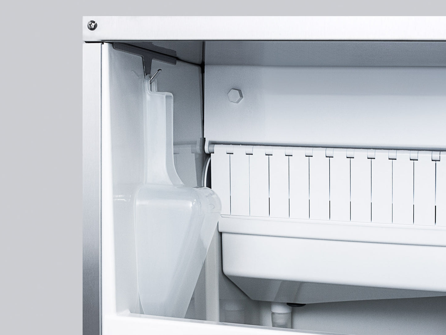 Interior view of clear ice maker with ice chute and white plastic components in kitchen appliance collection