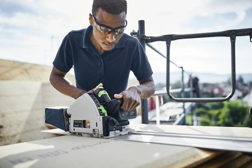 Person wearing safety glasses using Festool cordless track saw with 55-inch guide rail for woodworking outdoors