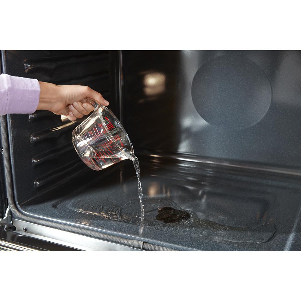 Hand pouring water inside a double wall oven cavity preparing for steam clean in kitchen appliance setting