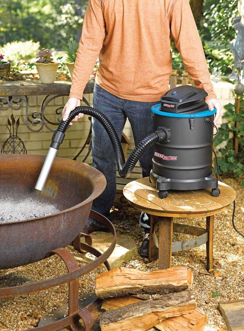 Black ash vacuum with blue rim and flexible hose cleaning ashes from outdoor fire pit for home improvement tasks