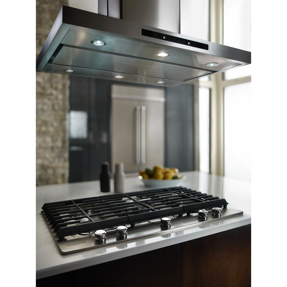 Modern stainless steel 30-inch gas cooktop with five burners and black grates under a sleek stainless steel vent hood in kitchen setting