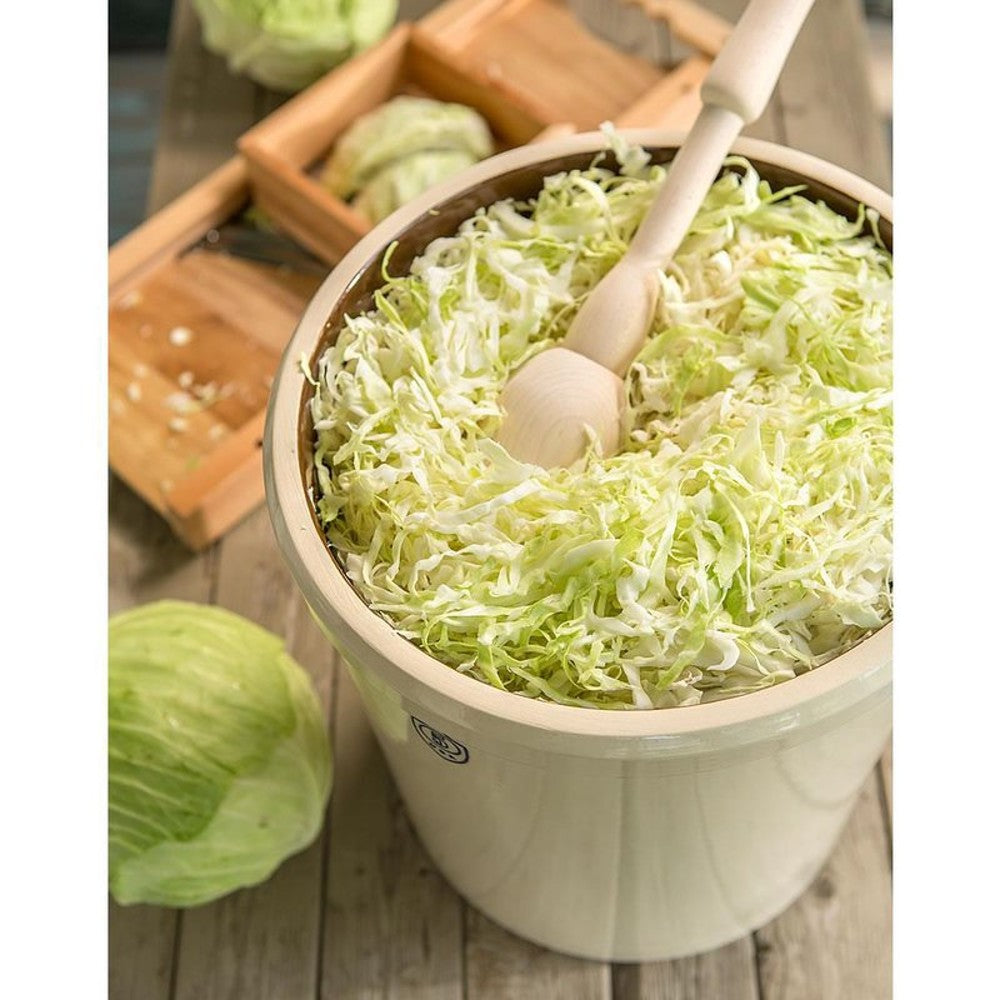 Cream-colored Ohio stoneware crock filled with shredded cabbage and wooden tamper for food preparation