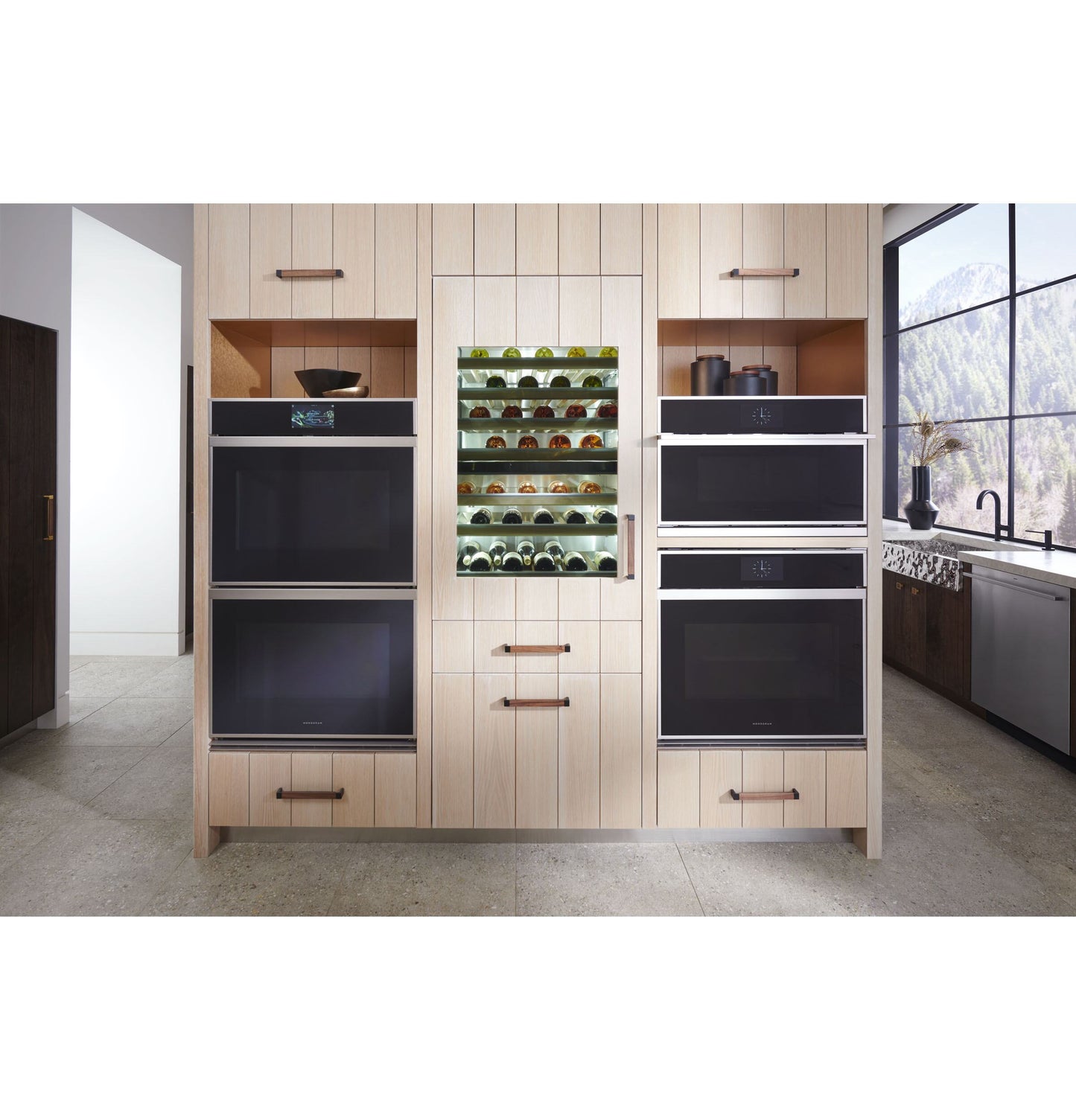 Built-in stainless steel wall ovens and wine cooler integrated into light wood cabinetry in modern kitchen setting