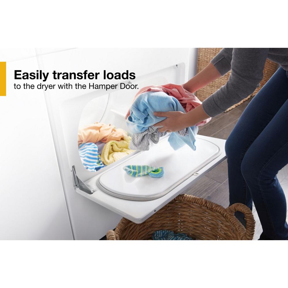 Person loading mixed laundry into a white top load gas dryer with an open hamper door in laundry room setting