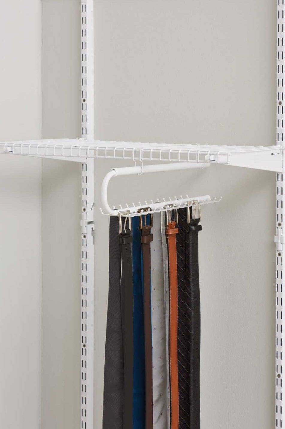 White metal tie and belt organizer hanging inside adjustable closet storage system with multiple belts displayed