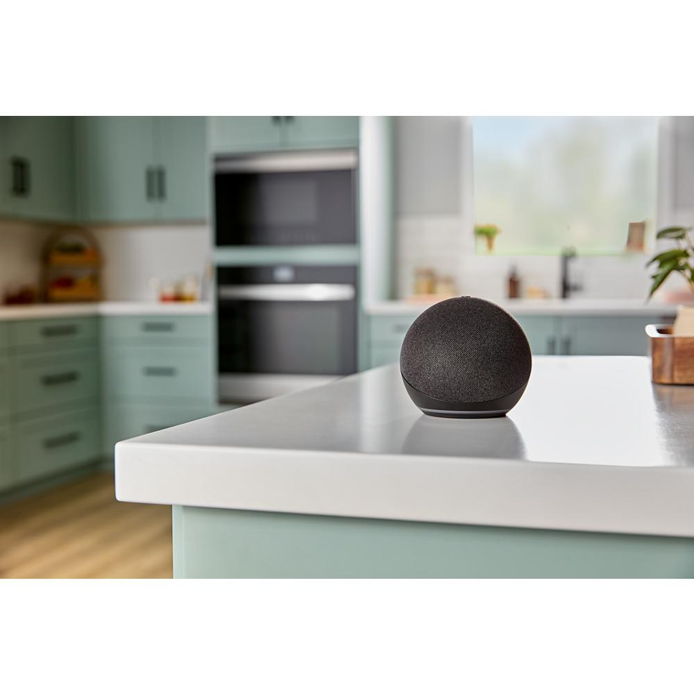 Compact smart speaker with rounded fabric design placed on kitchen island in modern kitchen with built-in appliances in background