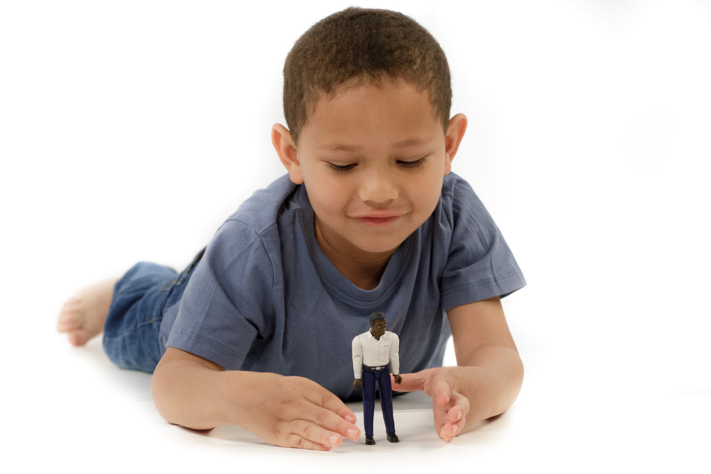 Young child lying on floor playing with dark-skinned articulated figure dressed in white shirt and dark blue jeans