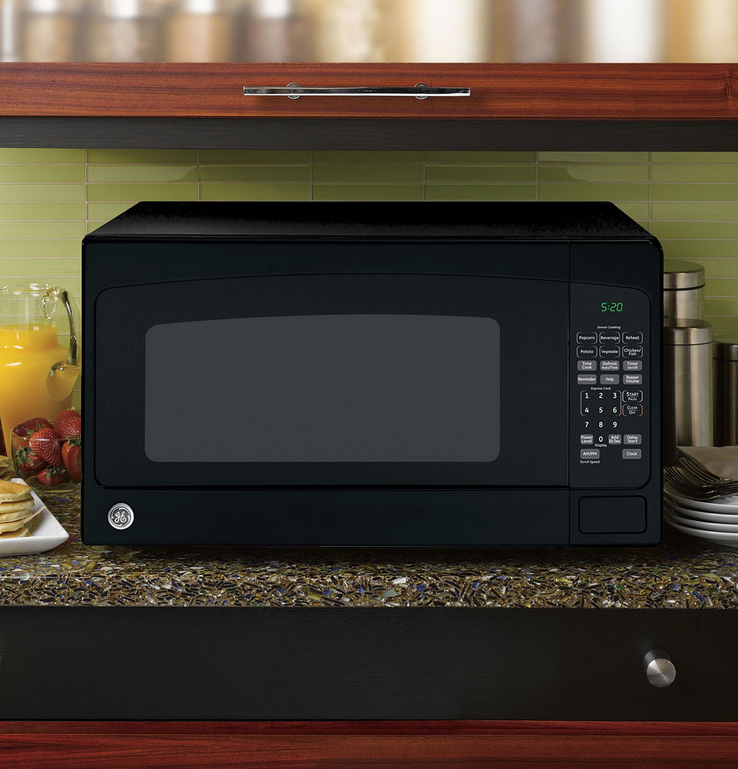 Black countertop microwave with digital keypad and green LED display on a kitchen counter with beverages and plates nearby