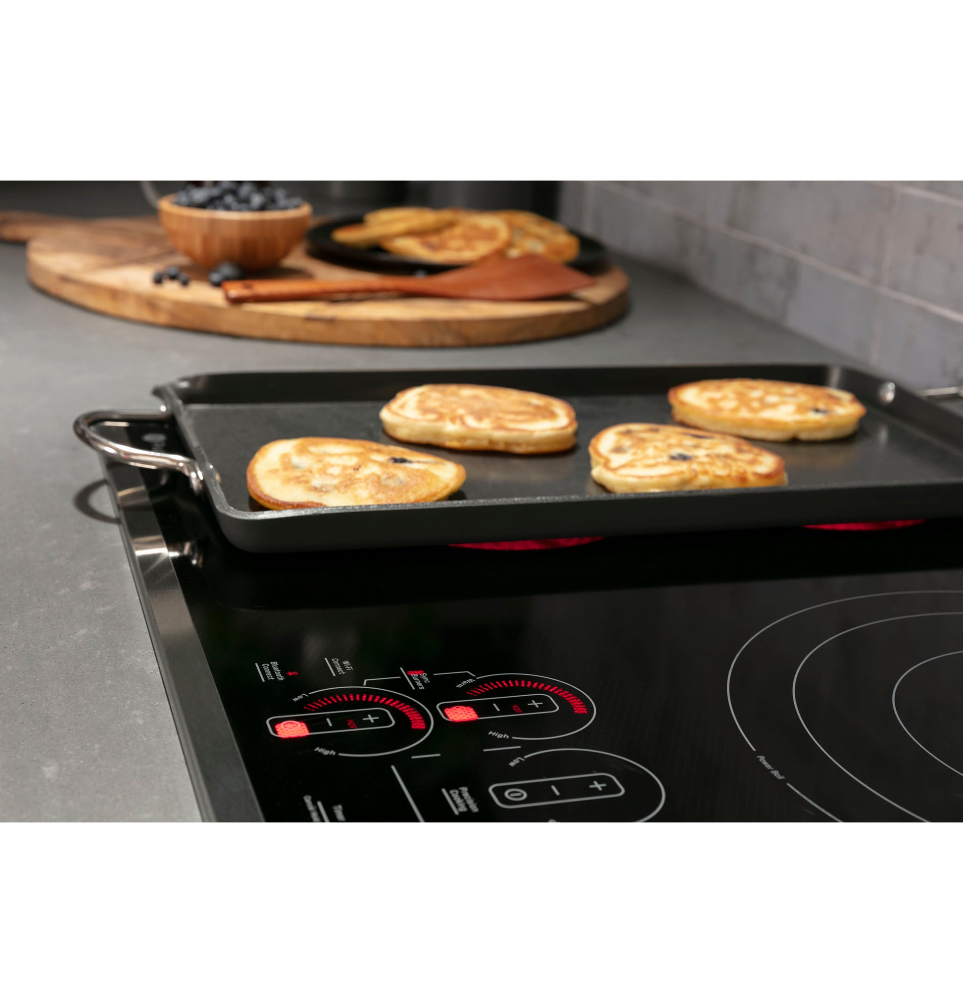 Close-up of black built-in cooktop with digital touch controls heating a griddle cooking pancakes in modern kitchen setting