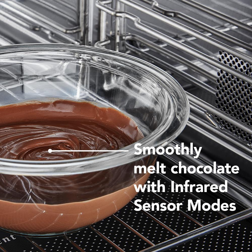 Glass bowl with melted chocolate inside a stainless steel multifunction microwave oven interior rack close-up view