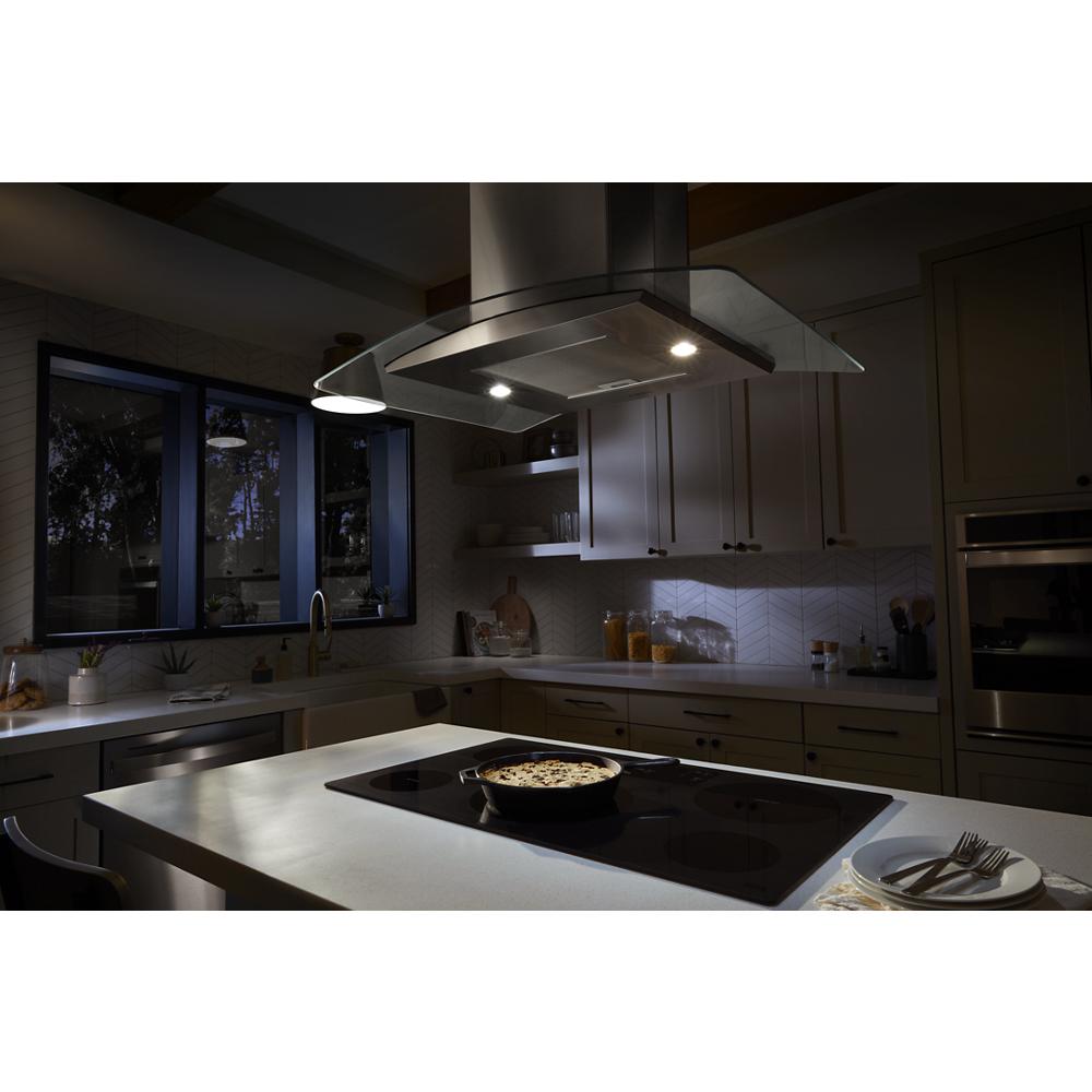 Modern kitchen island with stainless steel curved glass range hood and cooktop illuminated by built-in lights