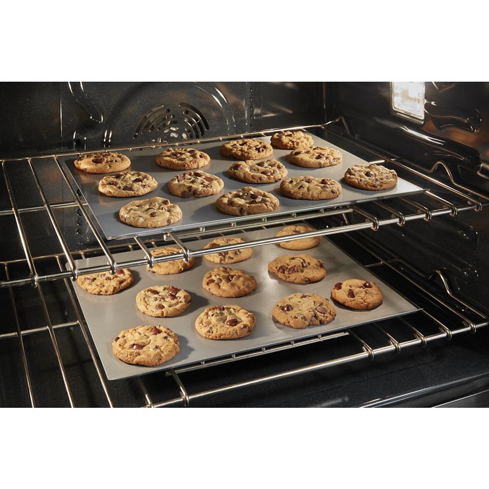 Two trays of chocolate chip cookies baking inside a stainless steel wall oven from the microwave combo collection