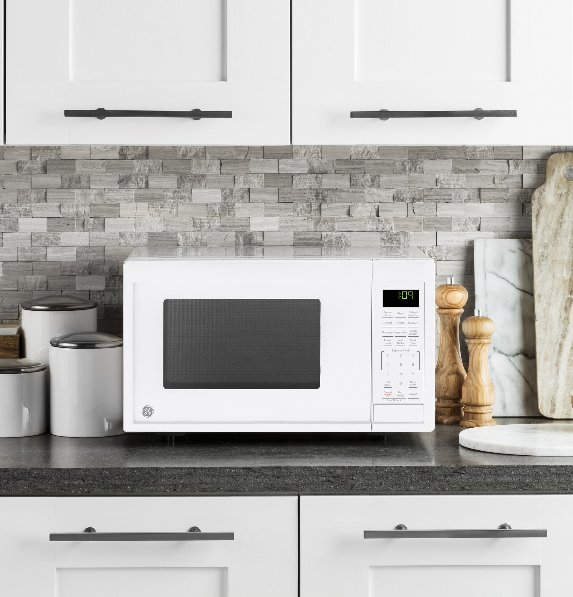 White countertop microwave oven with digital display and control panel in modern kitchen setting with stone backsplash