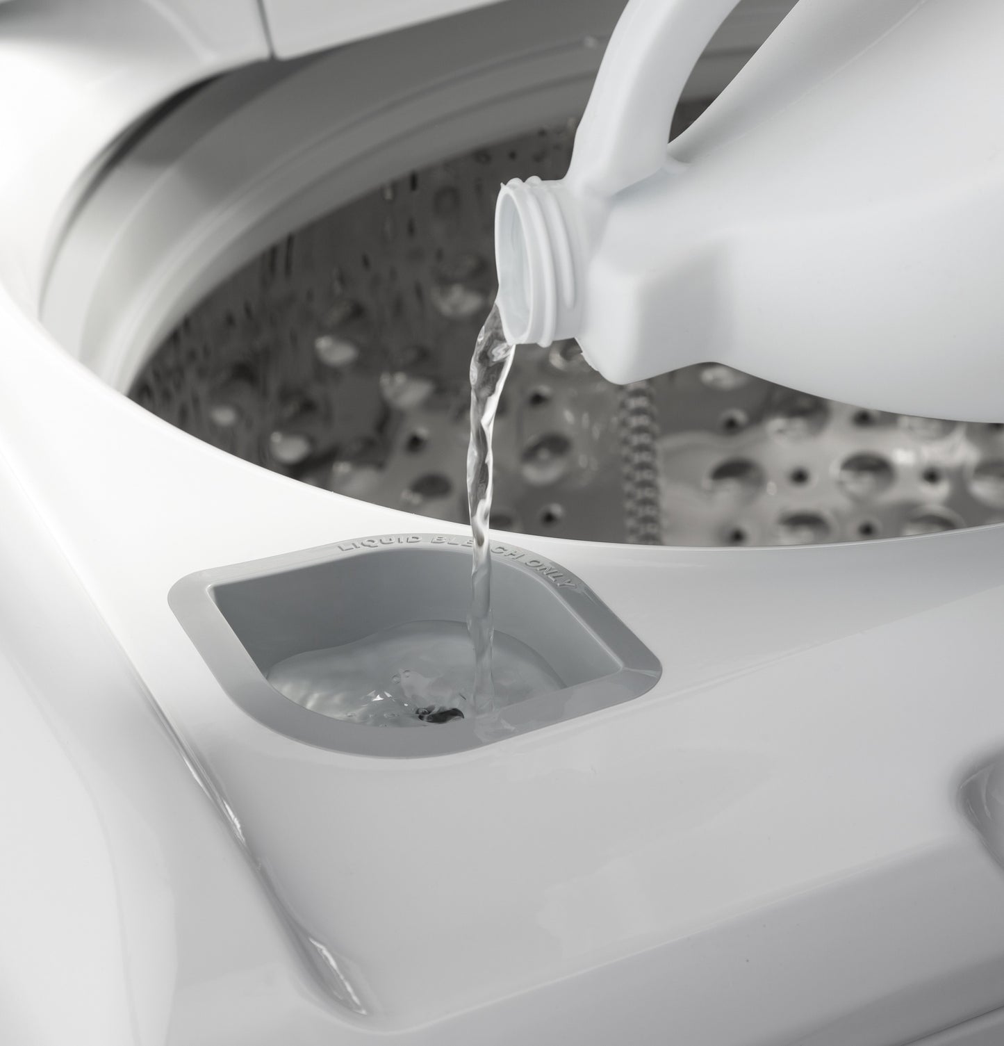 Close-up of top load washer detergent dispenser with liquid being poured into compartment from white bottle