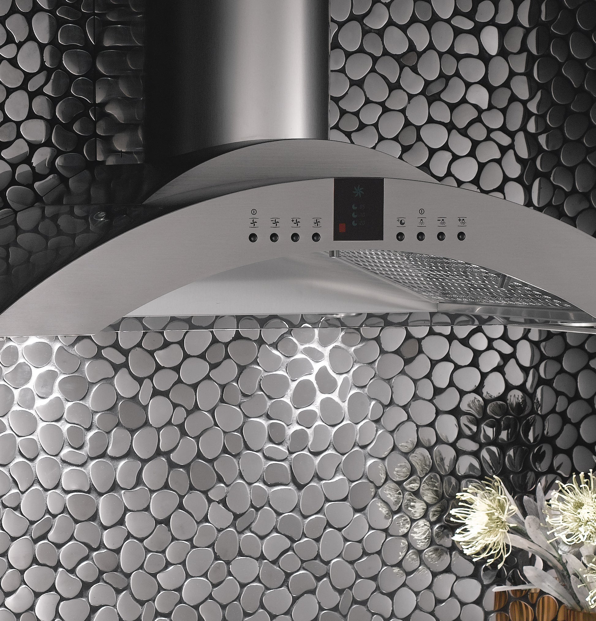 Curved stainless steel island vent hood with digital controls against pebble-textured wall in kitchen appliances collection