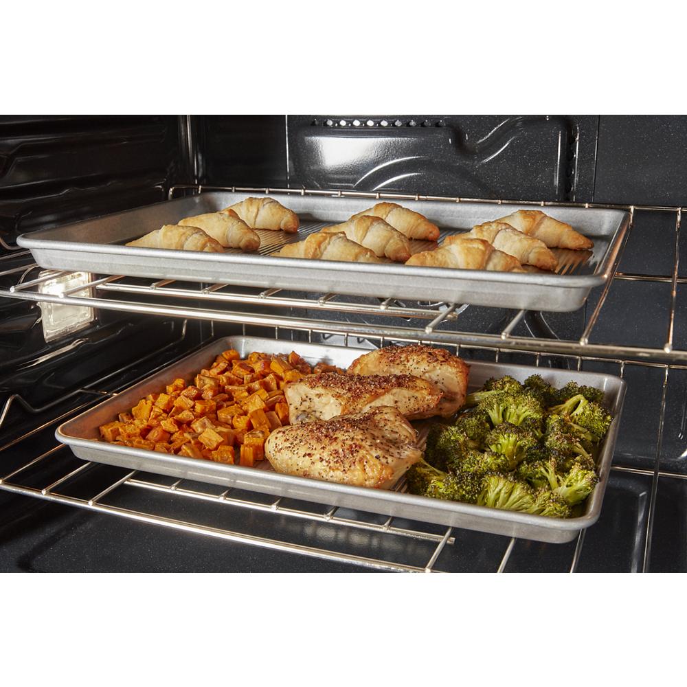 Two baking sheets cooking croissants, seasoned chicken, broccoli, and diced sweet potatoes inside a double wall oven from appliances collection