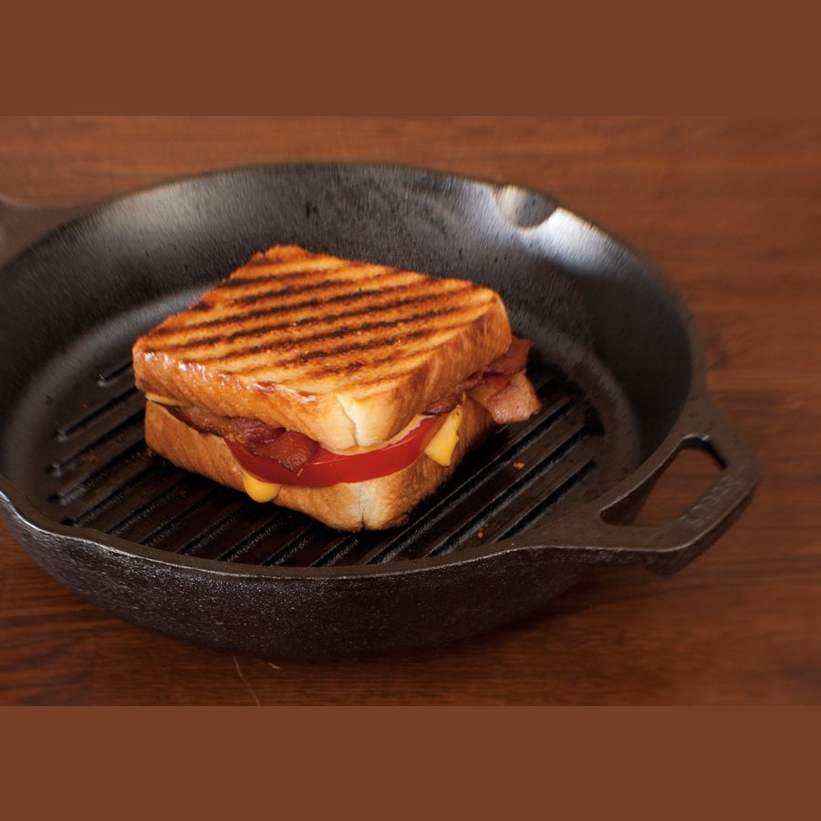 Black cast iron grill pan with ridged surface cooking a toasted sandwich on wooden tabletop under $50 kitchenware