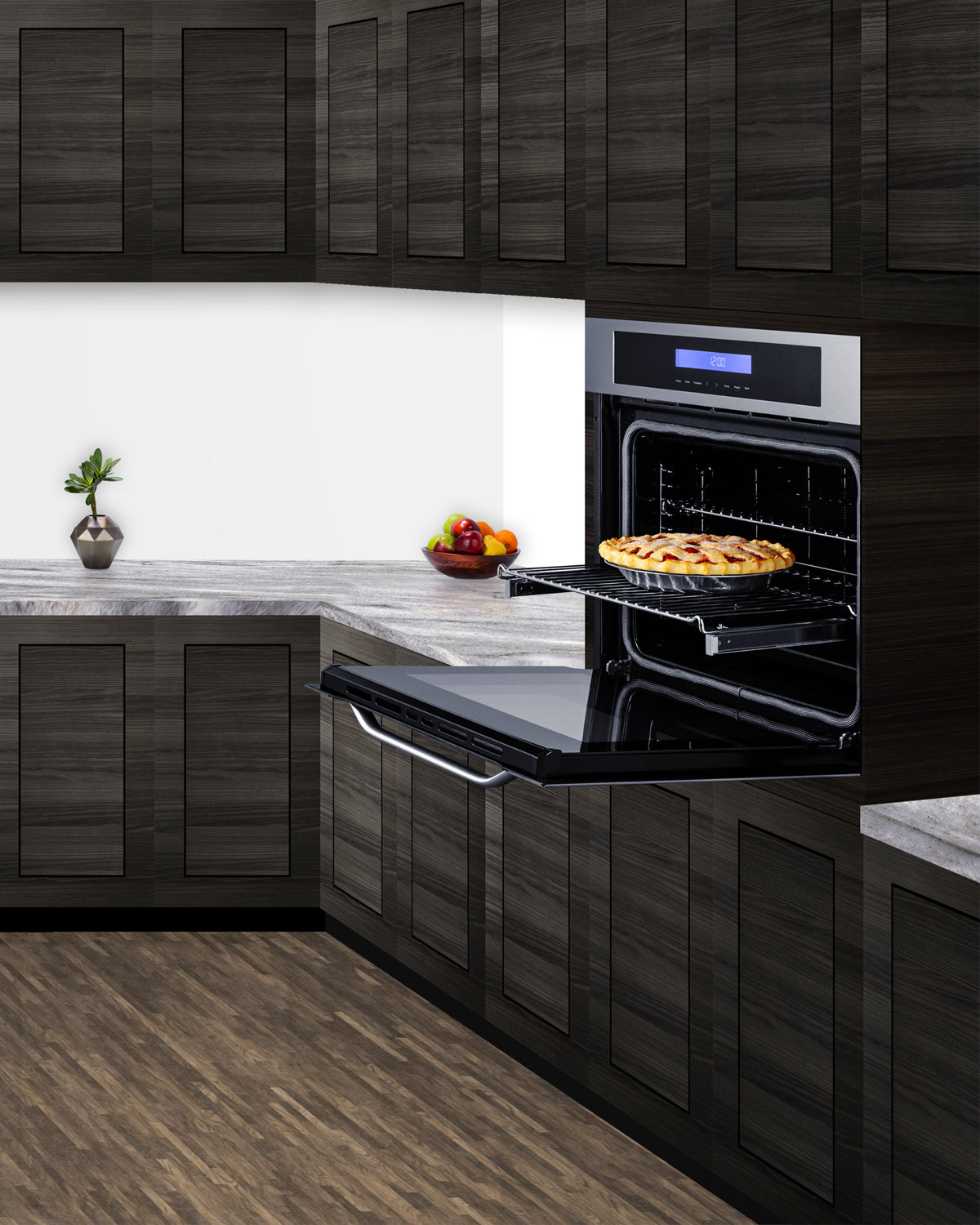 Electric wall oven with stainless steel finish and digital display, open in modern kitchen with pie inside and dark cabinetry