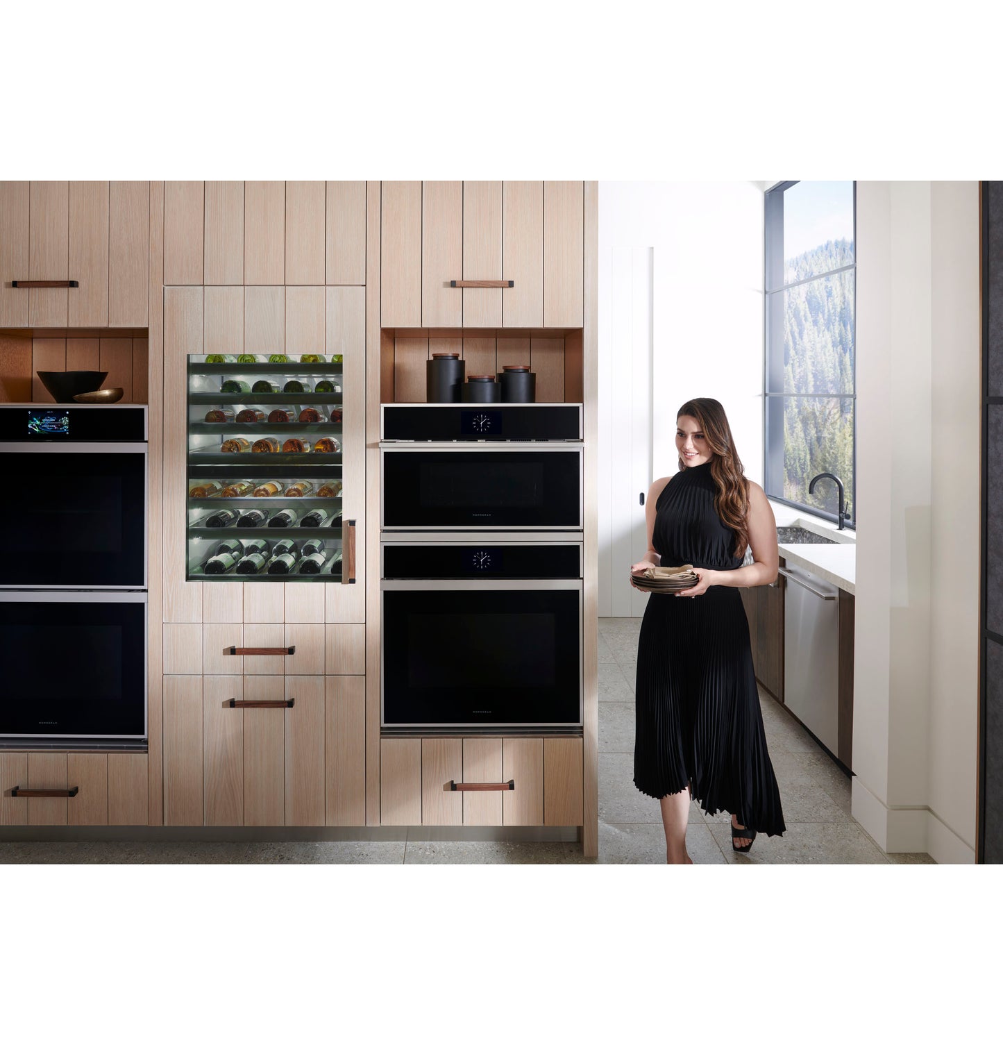 Modern kitchen featuring Monogram double wall ovens and built-in beverage fridge with woman holding a plate nearby