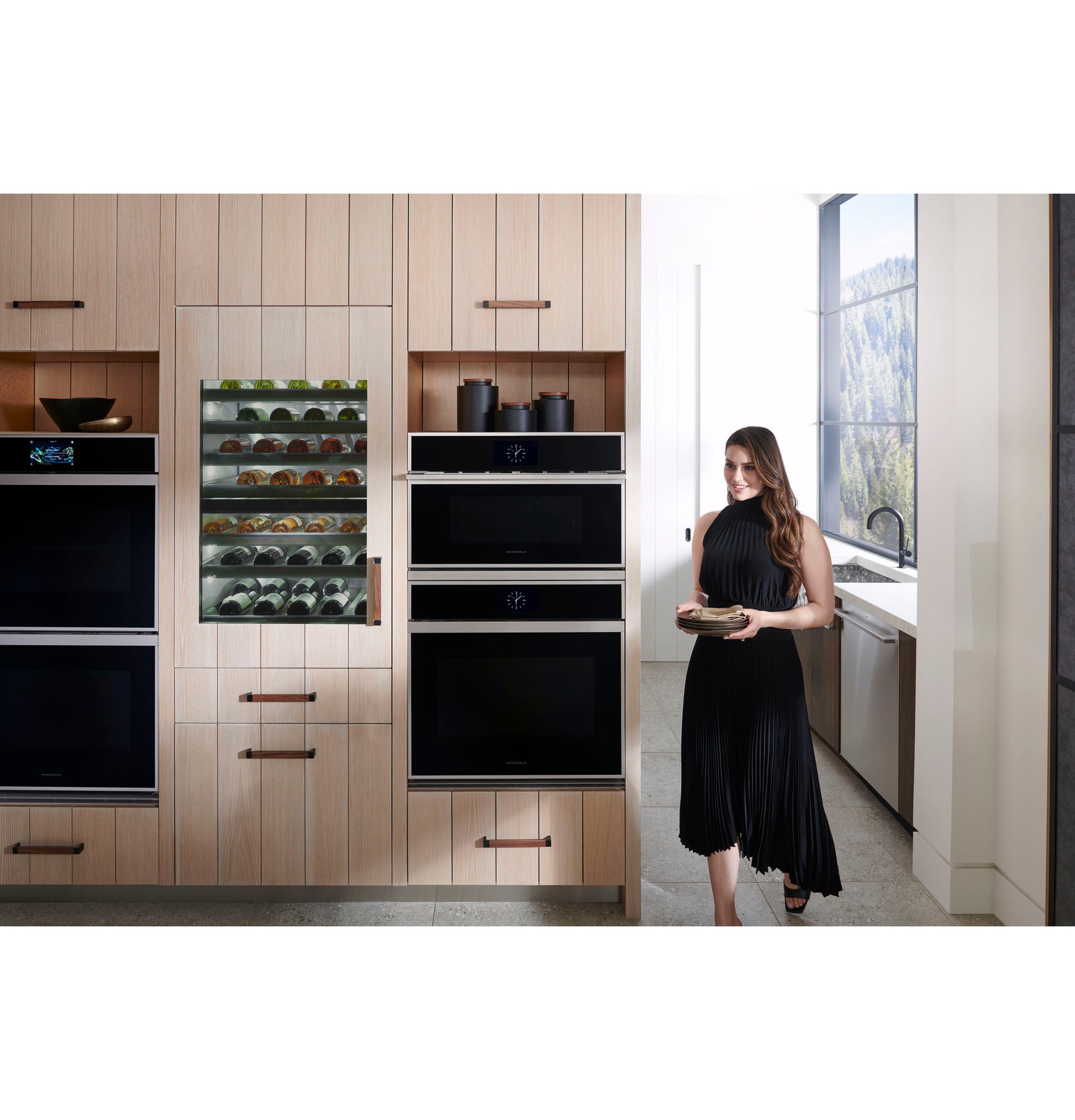 Modern kitchen featuring Monogram double wall ovens and built-in beverage fridge with woman holding a plate nearby