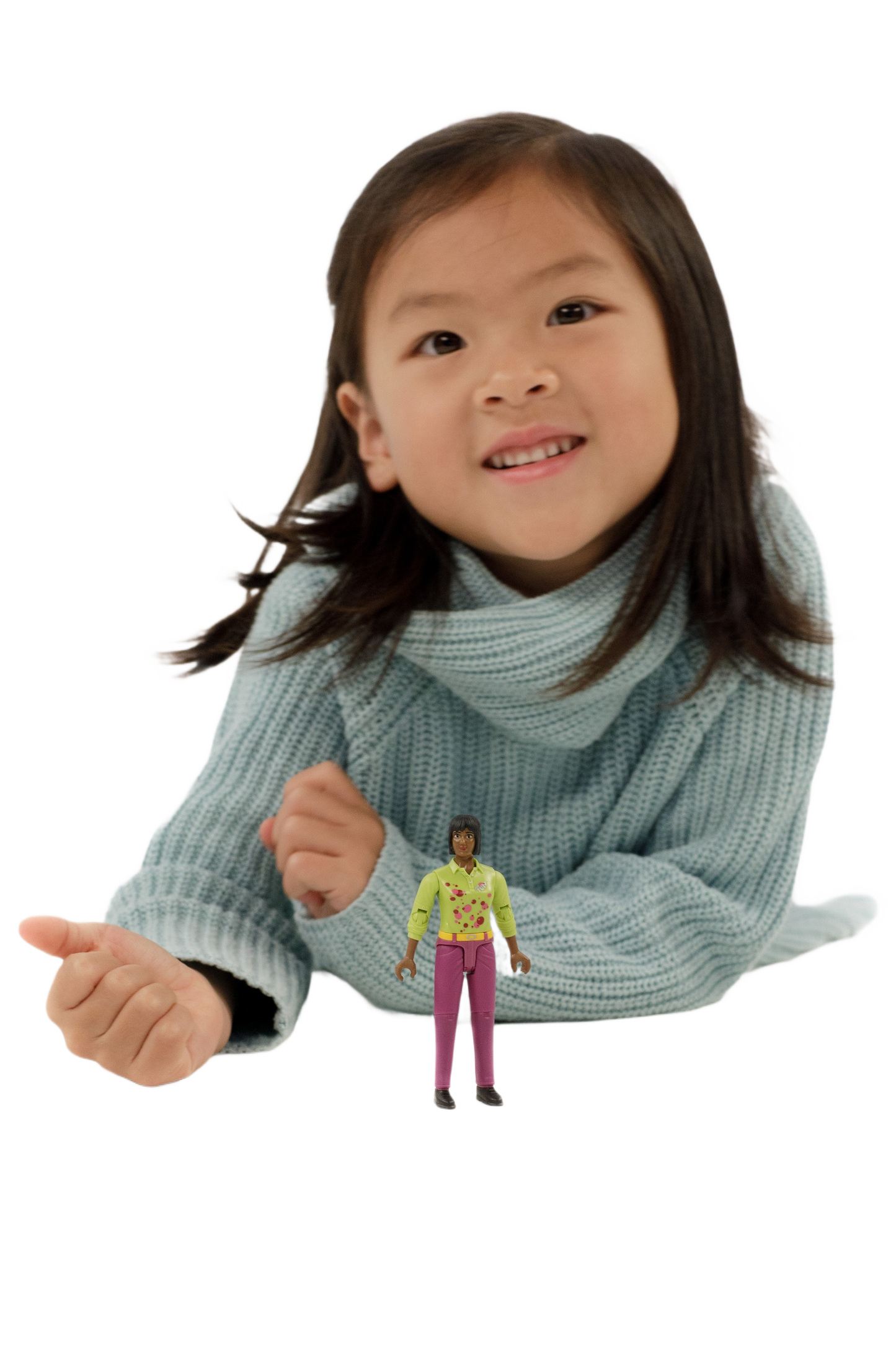 Young girl in blue sweater smiling behind a small toy figure of a woman wearing pink pants and a yellow top