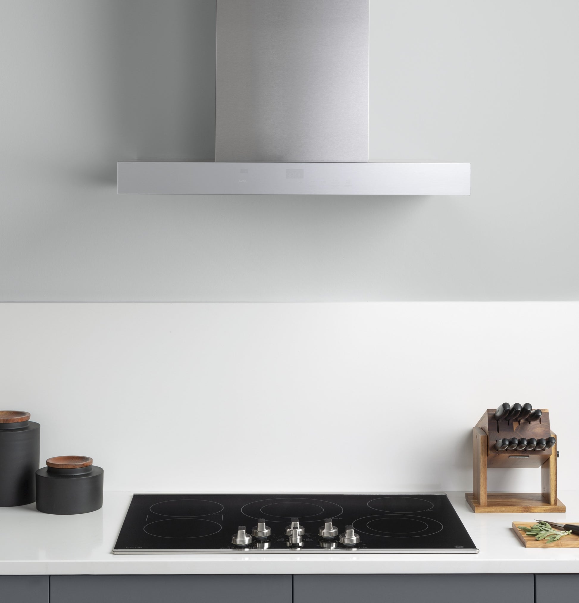 Modern stainless steel wall mount range hood with perimeter venting above black glass cooktop, kitchenware and appliances collections