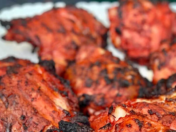Close-up view of several pieces of marinated chicken cooking on a grill with charred edges and a rich, reddish color.