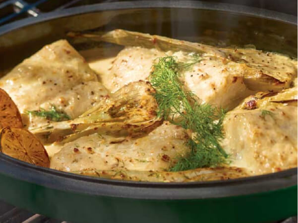 Close-up of chicken pieces cooking in a pan with fennel slices and fresh dill, showing a lightly browned surface and herbs.