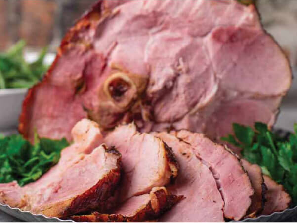 Close-up of sliced ham with a browned crust arranged on a bed of fresh green leafy garnish.
