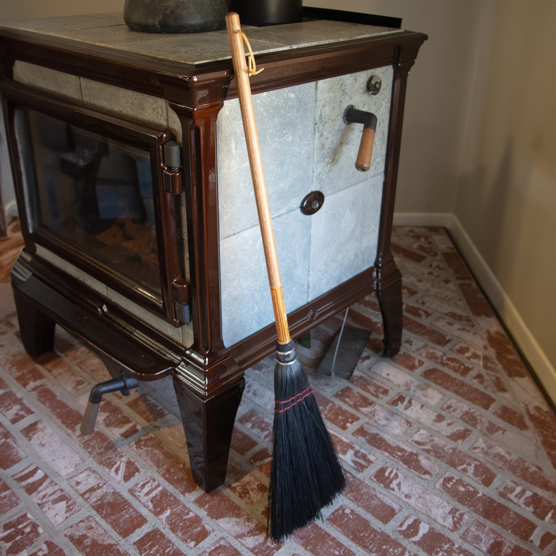 Black bristle broom with wooden handle resting against a wood stove, part of Cleaning Tools and Brooms & Dust Pans collections