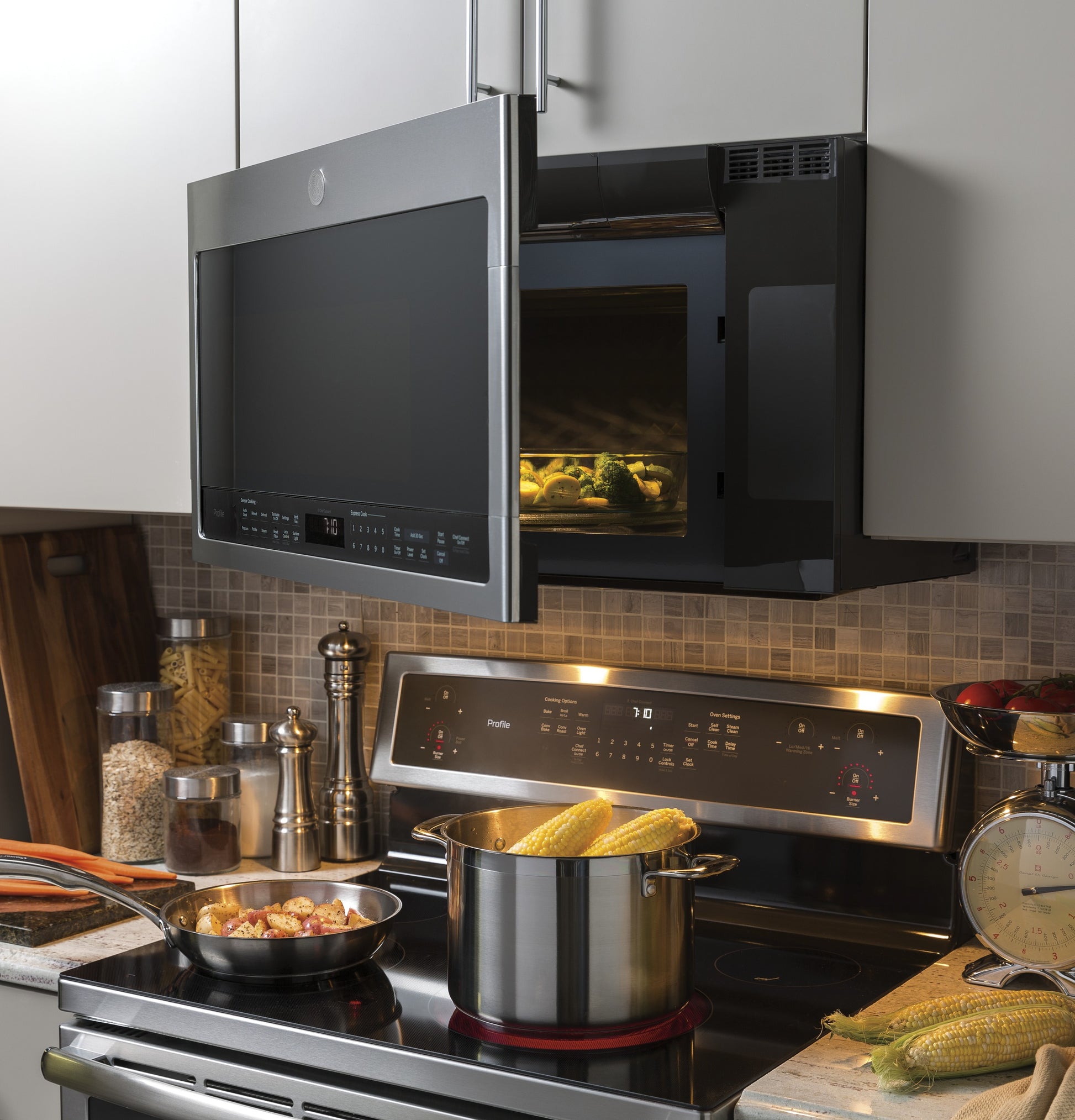 Stainless steel sensor over-the-range microwave with digital controls above electric stove in modern kitchen setup