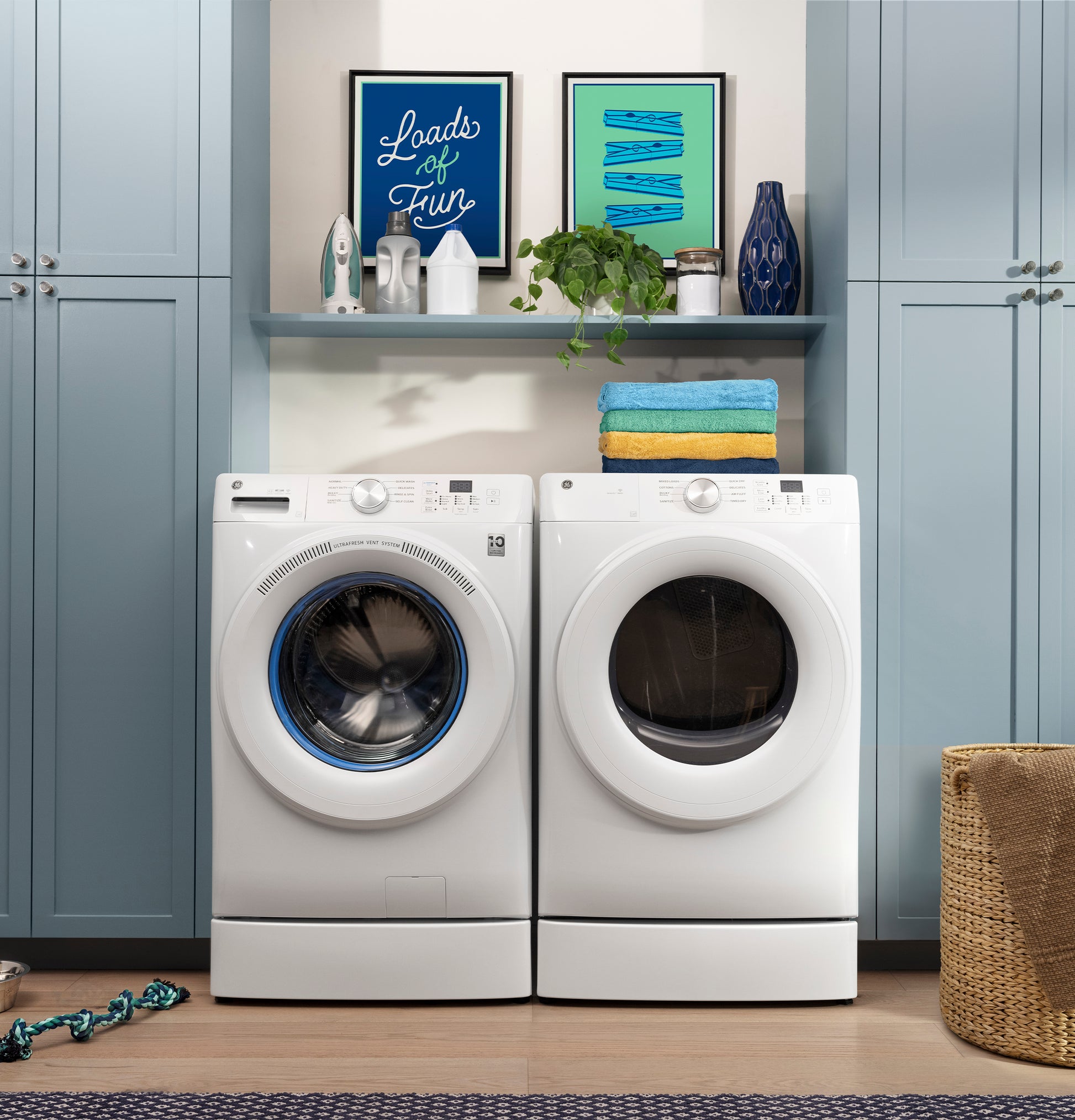 White front load washer and smart gas dryer set with folded towels and decorative shelf in modern laundry room