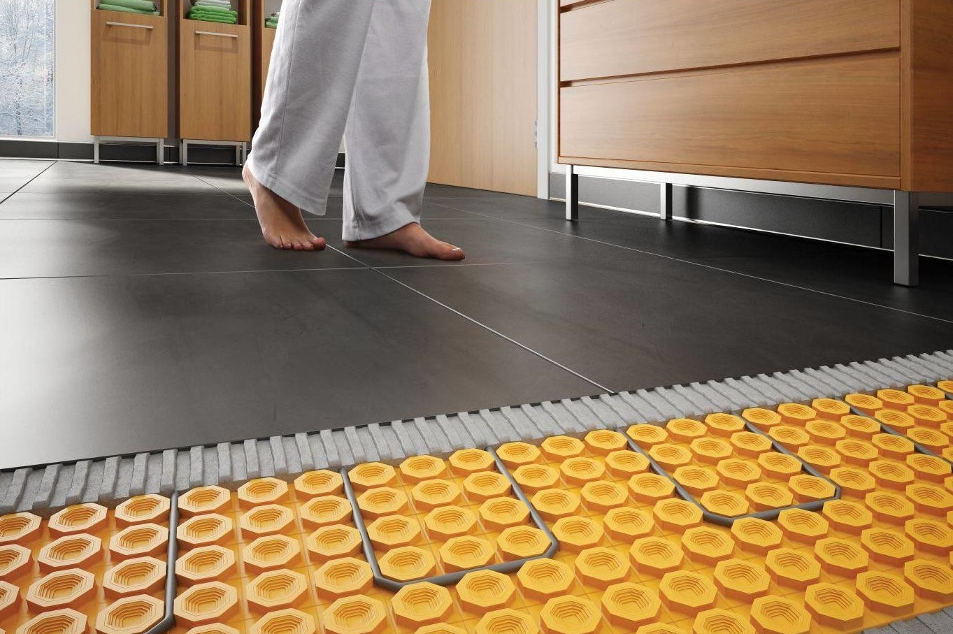 Person walking barefoot on black tile flooring with electric floor heating membrane exposed under tiles in modern kitchen
