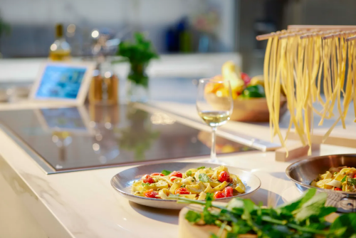 Dark gray induction cooktop with frame on kitchen island featuring pasta dishes and glass of white wine nearby