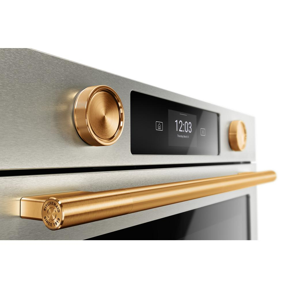 Close-up of a smart electric wall oven with brushed gold knobs and handle in modern kitchen appliance setting