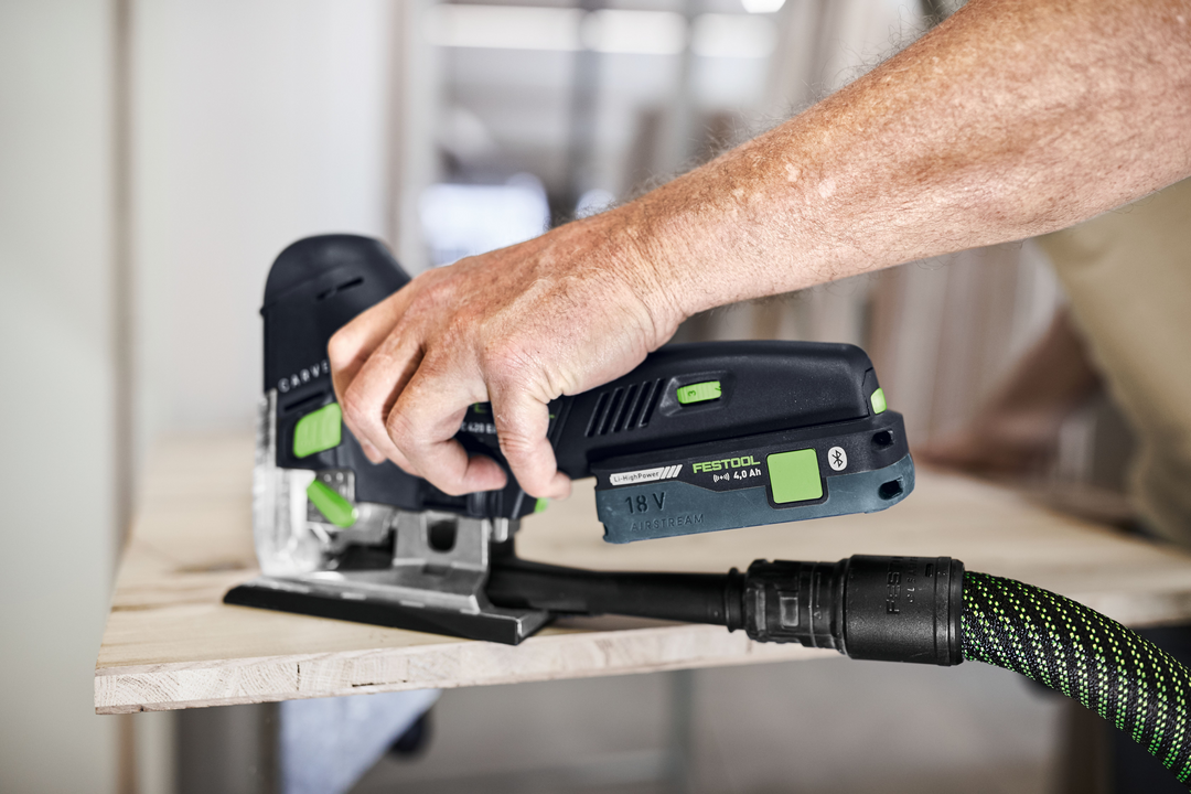 Handheld Festool cordless barrel grip jigsaw cutting wood with dust extraction in a workshop setting