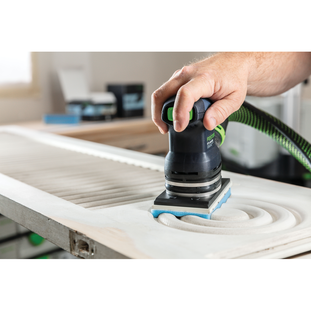 Person using compact power sander with blue foam-backed abrasive on decorative woodwork in home improvement setting